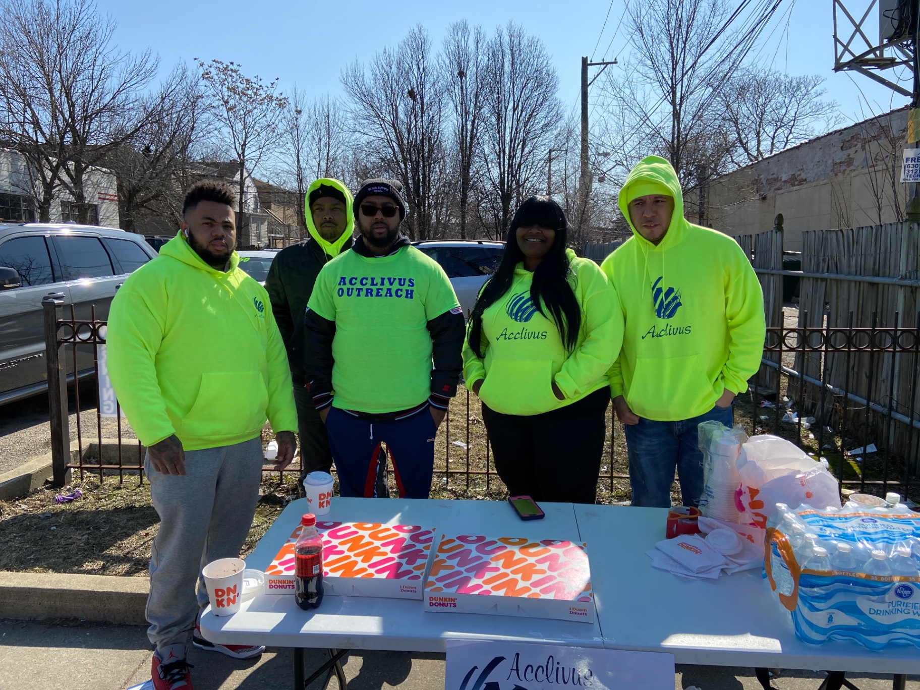 The outreach team standing behind a table of coffee, donuts, and water on a sunny morning